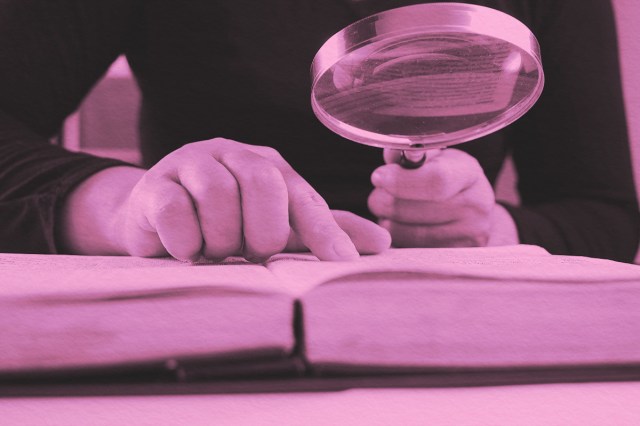 Close-up of a woman looking through a magnifying glass at a dictionary