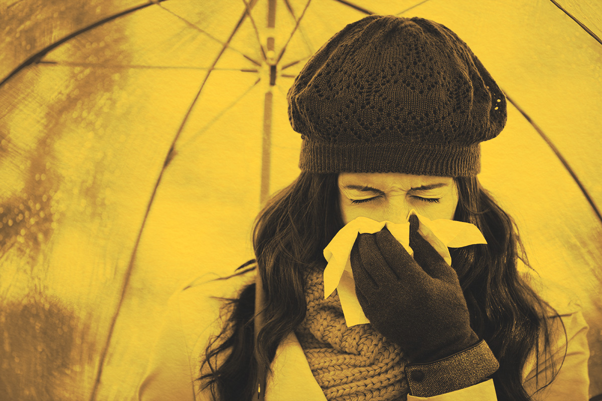 Woman with cold or flu coughing and blowing her nose with a tissue under her umbrella