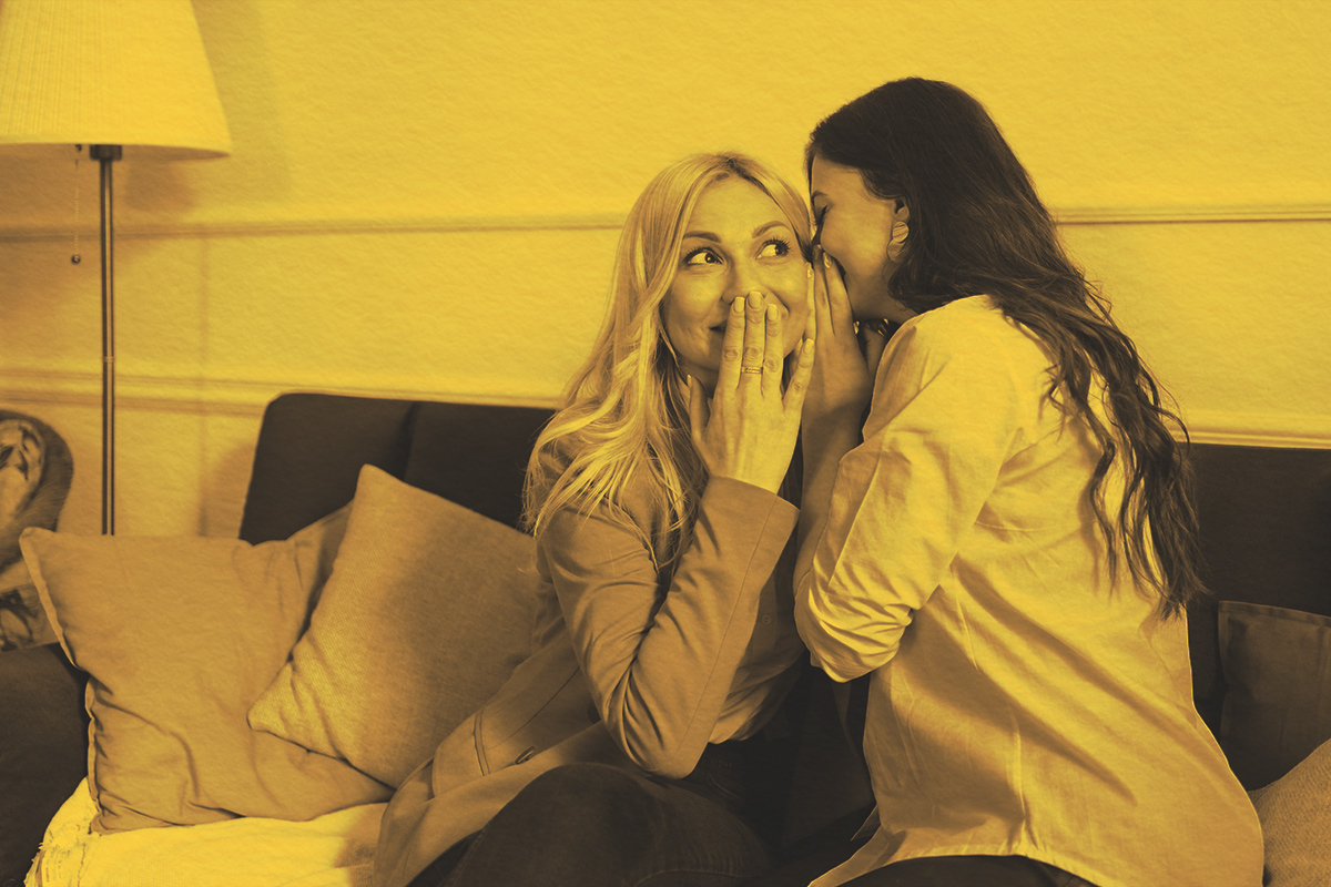 Two people whispering to one another on a couch